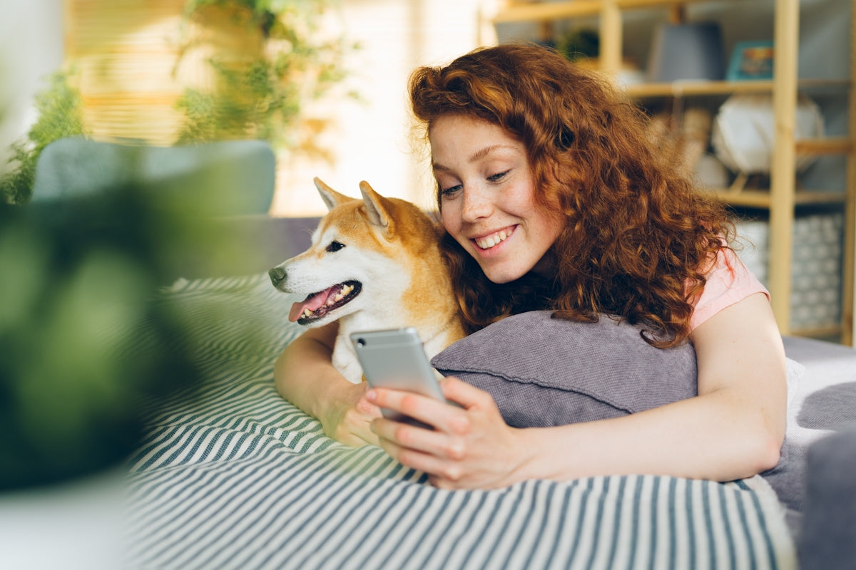 a woman laying on a bed with a dog looking at a cell phone