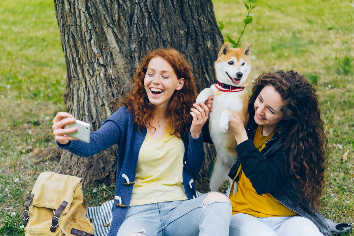 two women sitting next to a tree with a dog
