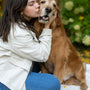 A woman sitting on the ground kissing a dog
