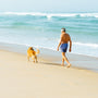 man in blue board shorts with dog walking at the shore