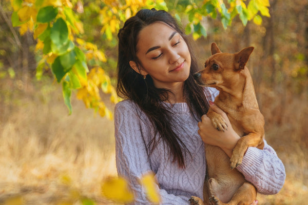 woman in gray long sleeve shirt carrying brown short coated dog during daytime