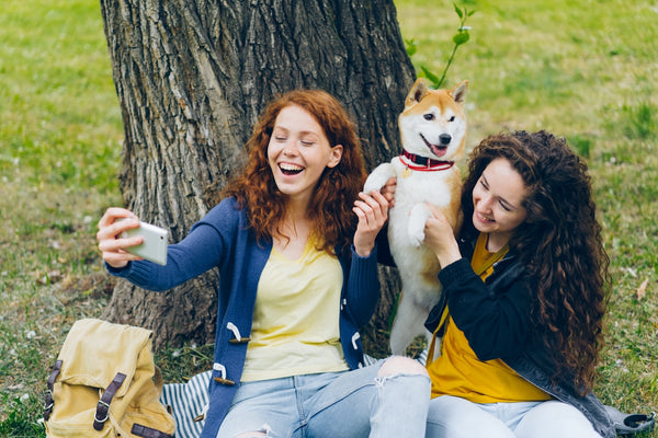 two women sitting next to a tree with a dog